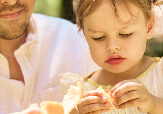 A preschooler and her dad peel an orange together.