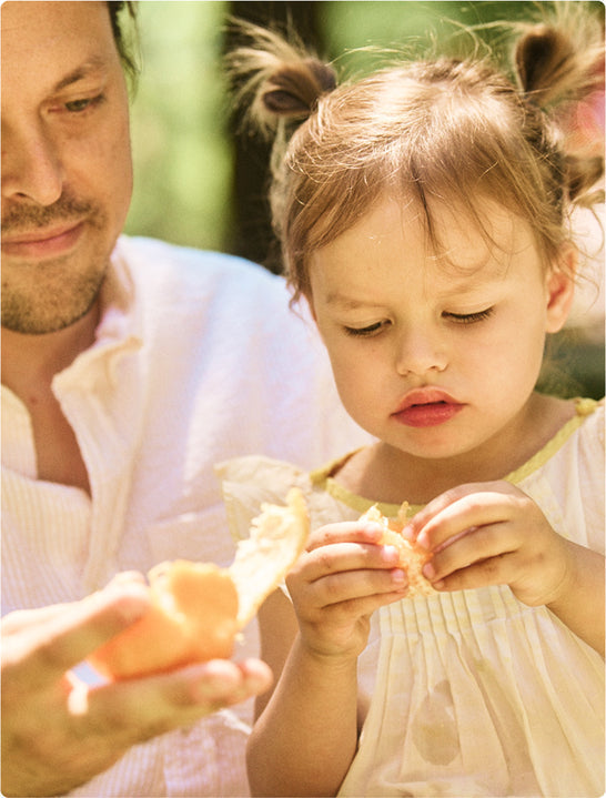 A preschooler and her dad peel an orange together.
