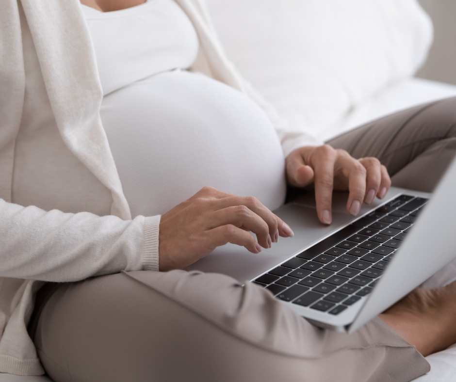 A pregnant woman types on her laptop.