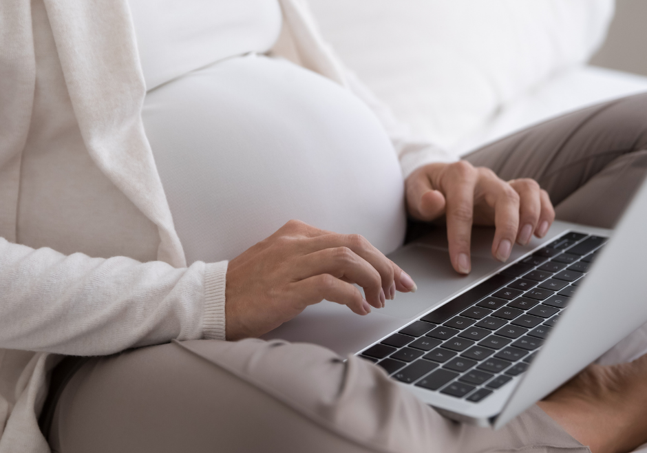 A pregnant woman types on her laptop.