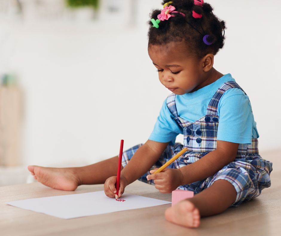 A toddler girl drawing with map pencils with both hands.