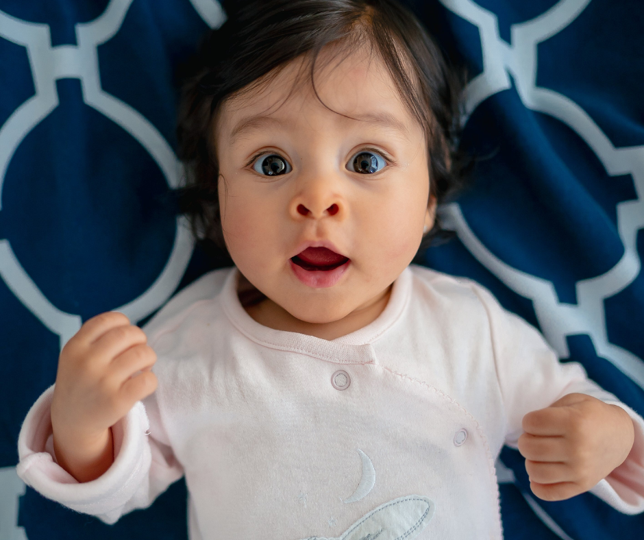 A wide-eyed infant girl waking up in her crib.