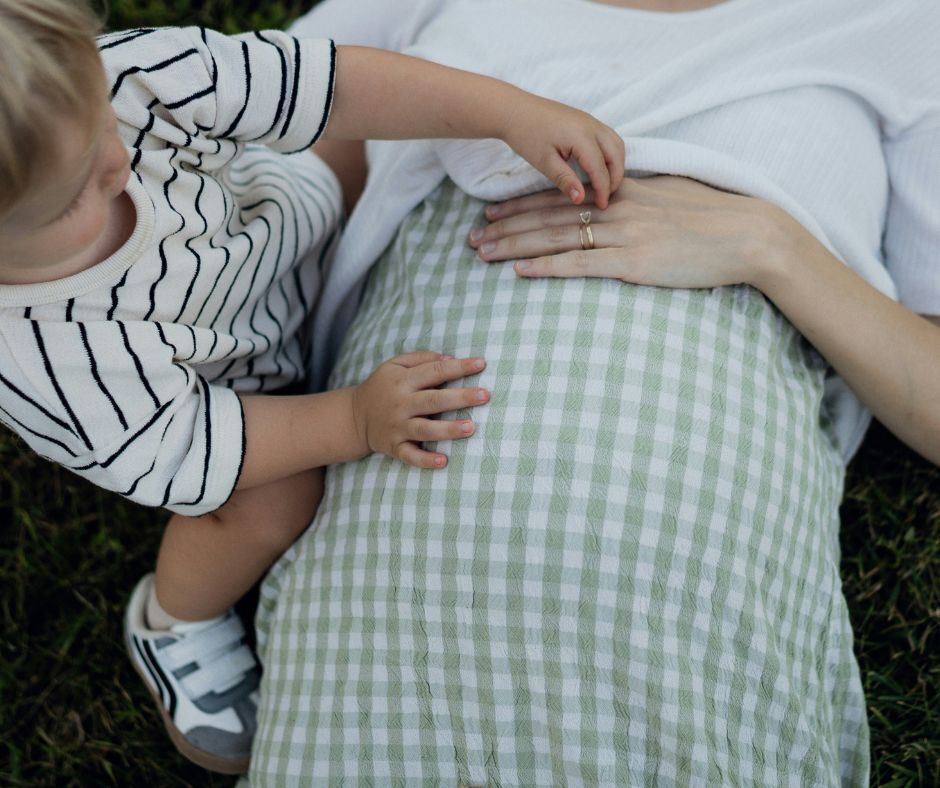 A toddler boy touches his pregnant mom's belly.