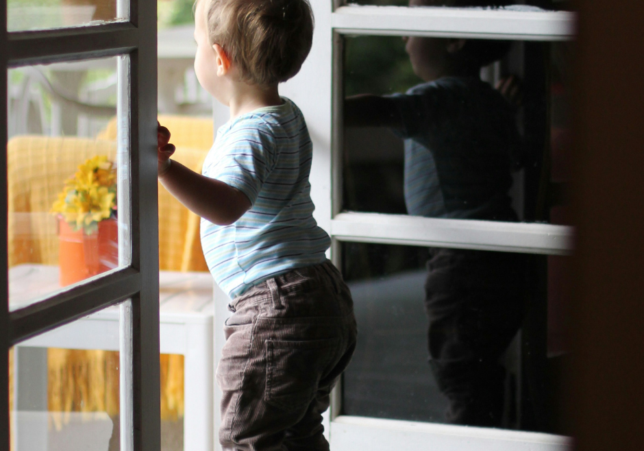 A toddler boy peeks outside during spring.