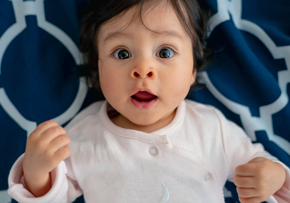 A wide-eyed infant girl waking up in her crib.