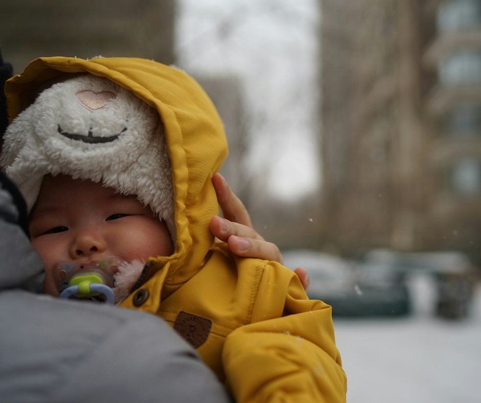 A sick baby all bundled up for cold weather snuggles on their parent's shoulder