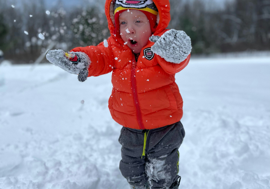 A toddler in warm winter clothes plays in the snow.