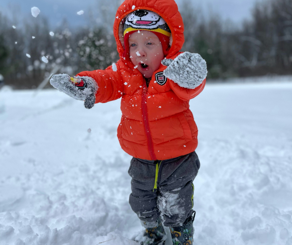 A toddler in warm winter clothes plays in the snow.