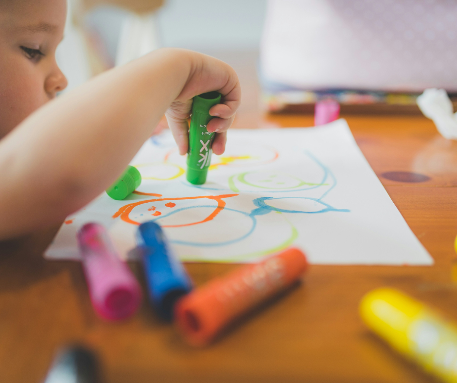 A toddler plays independently with crayons and paper.