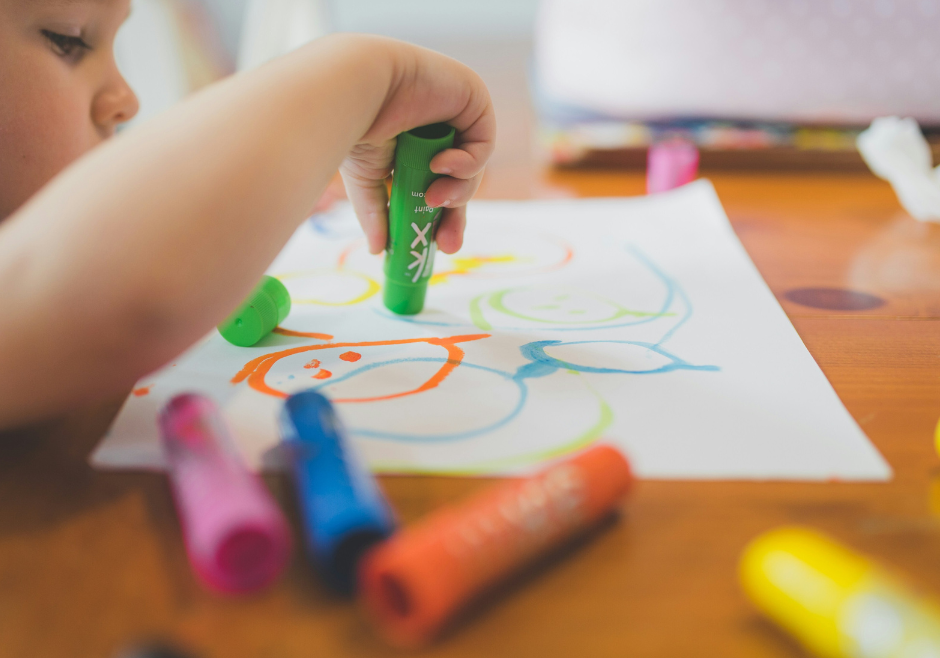 A toddler plays independently with crayons and paper.