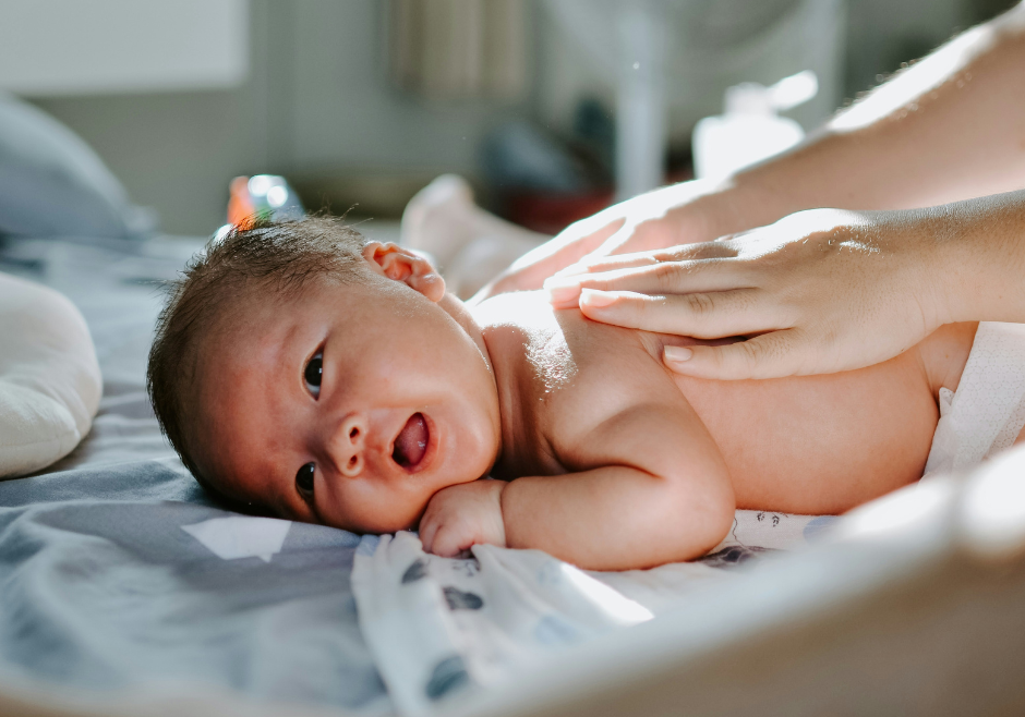 A young baby on his tummy getting his bare back rubbed. 