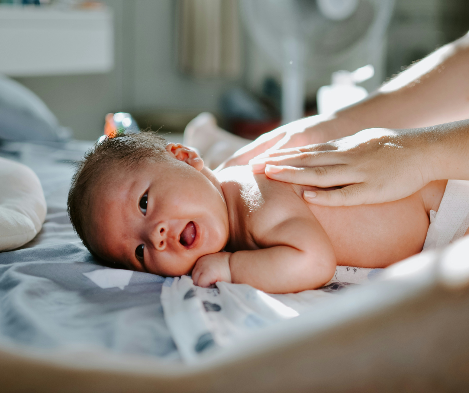 A young baby on his tummy getting his bare back rubbed. 