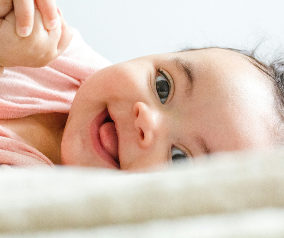 A smiling infant with a healthy skin microbiome wearing a pink onesie.
