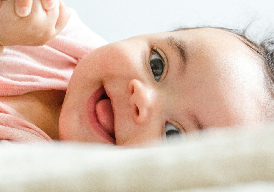 A smiling infant with a healthy skin microbiome wearing a pink onesie.