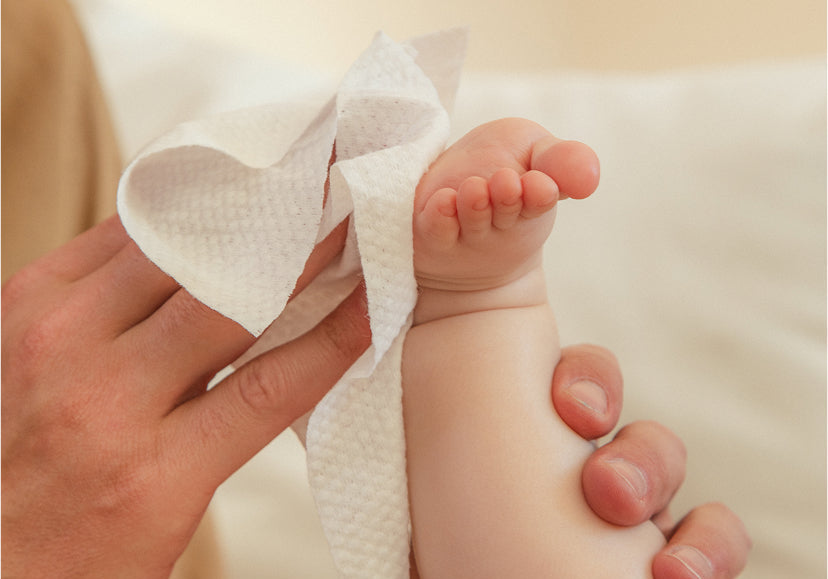 A parent wipes a baby's foot with a wet wipe after a diaper change.