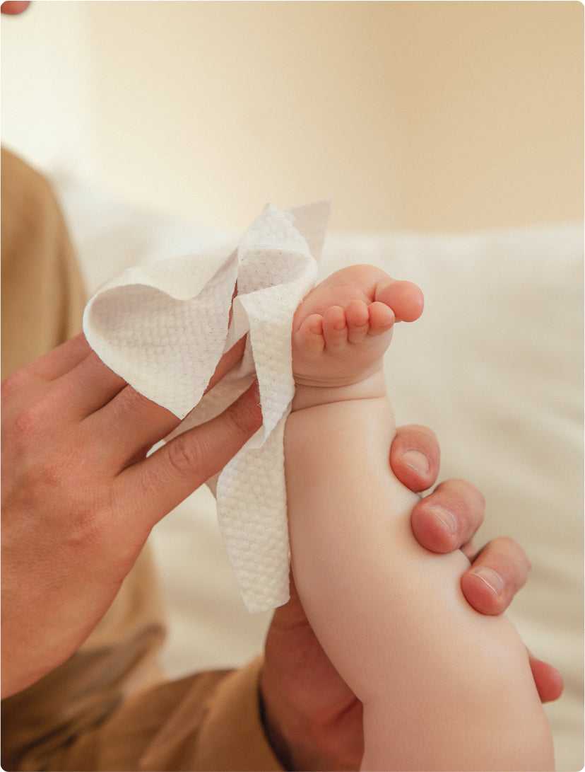 A parent wipes a baby's foot with a wet wipe after a diaper change.