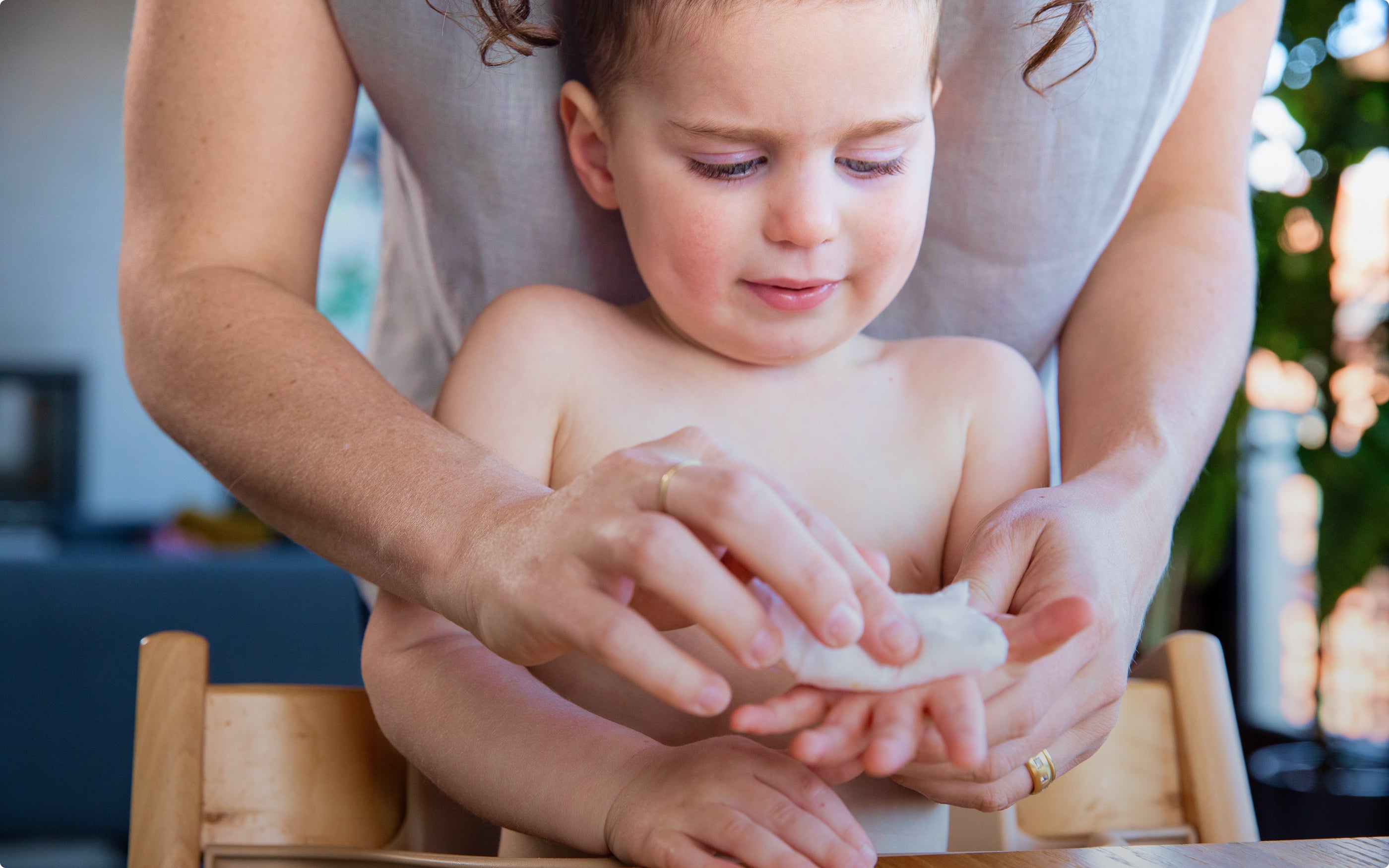A child sitting in a high chair with an adult cleaning their hands with a wet wipe.